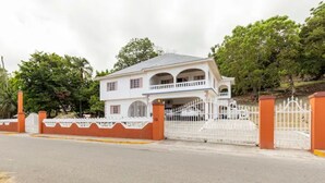 A two-story house with a balcony, surrounded by a white fence and orange pillars. - Shaw Park Gem (Ocho Rios)