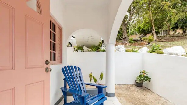 A blue Adirondack chair outside a building with a pink door. - Shaw Park Gem (Ocho Rios)