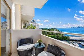 A balcony with wicker furniture, a potted plant, and a view of the city skyline and water. - Waterfront Cozy Studio with a View (North Bay Village)