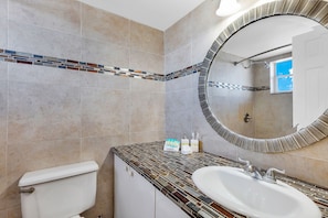 A bathroom with a tiled floor, a toilet, a sink, and a mirror.