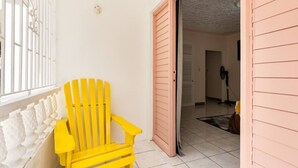 Una silla amarilla en un pasillo con una puerta rosa y suelo de baldosas.