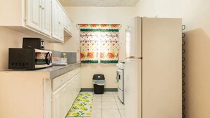 Una cocina compacta con gabinetes blancos, un microondas, una estufa y un refrigerador.