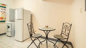 Una cocina pequeña equipada con refrigerador, estufa y microondas. Hay una mesa redonda con dos sillas.