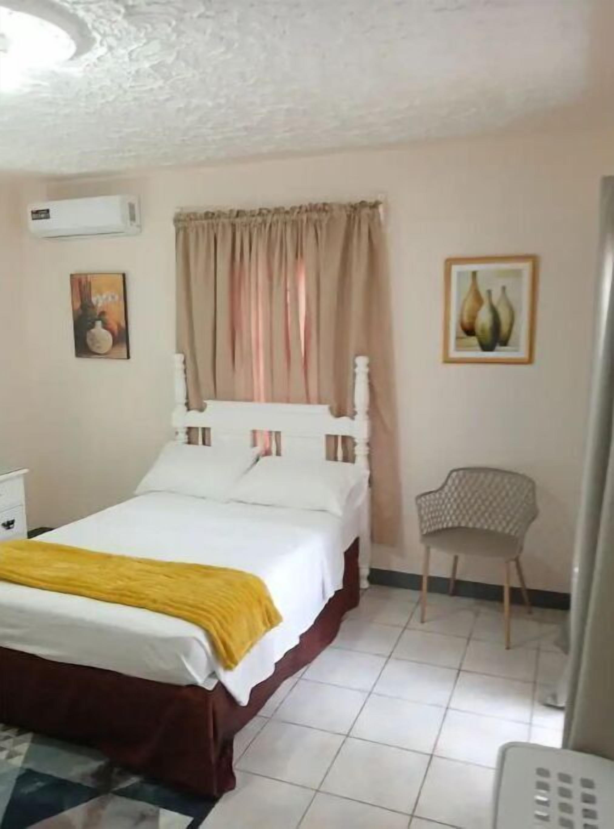 A bedroom with a bed, a chair, a wall-mounted air conditioner, and a painting.