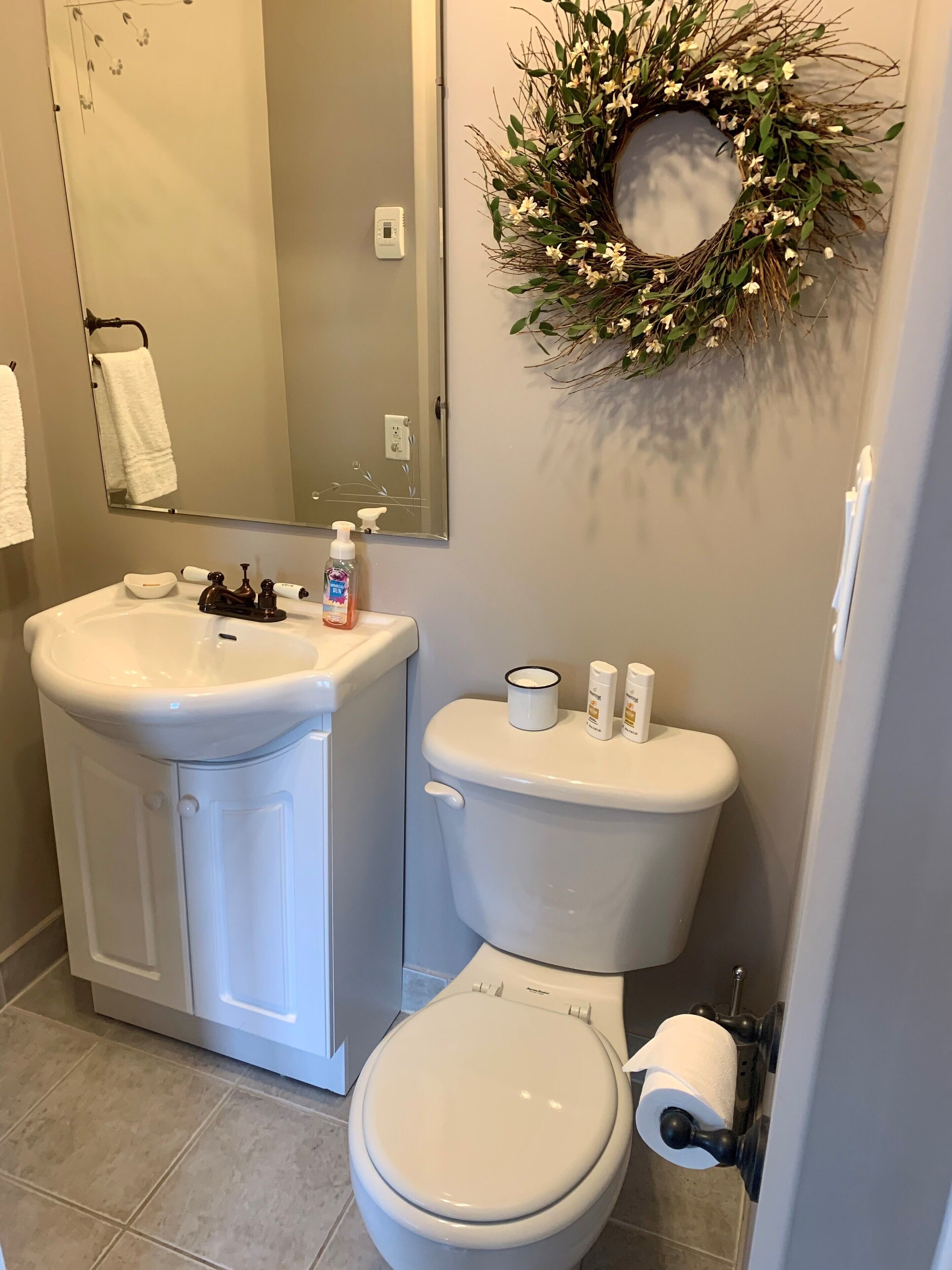 Un baño con lavabo blanco, espejo, inodoro y un arreglo decorativo en la pared.