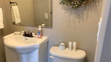 Un baño con lavabo blanco, espejo, inodoro y un arreglo decorativo en la pared.