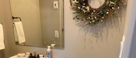 Un baño con lavabo blanco, espejo, inodoro y un arreglo decorativo en la pared.