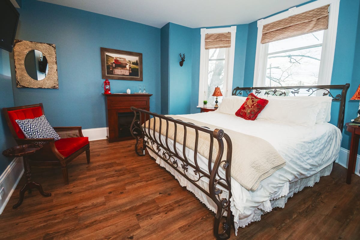 A bedroom with a wooden bed, a red chair, a fireplace, and a window with a view.