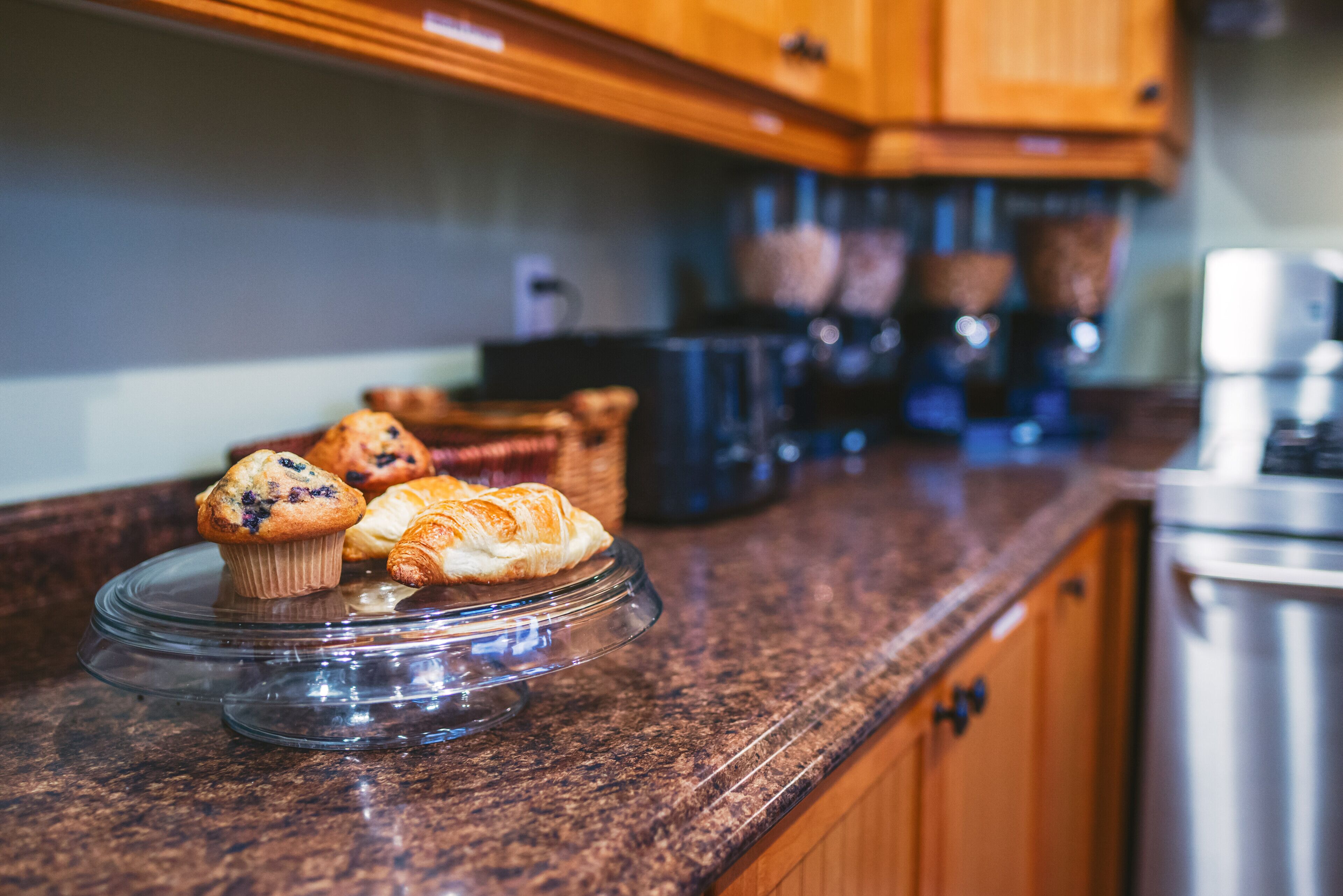 A kitchen counter with a glass display case containing muffins and croissants.