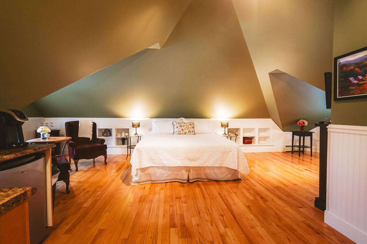 A bedroom with a sloped ceiling, a bed, a chair, and bedside tables with lamps.