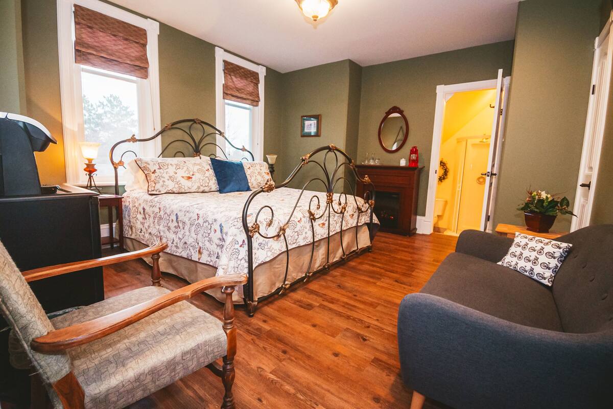 A bedroom with a bed, a chair, a sofa, a dresser, and a window with blinds.