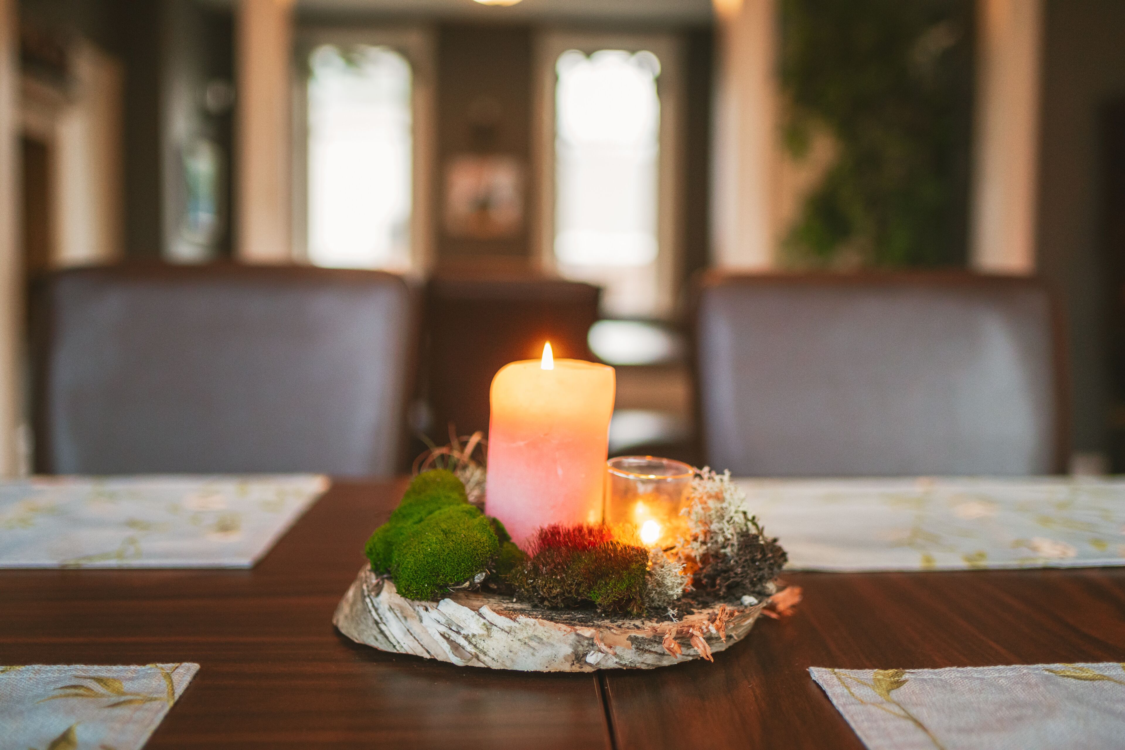 A candle on a table with moss and a glass candle holder.