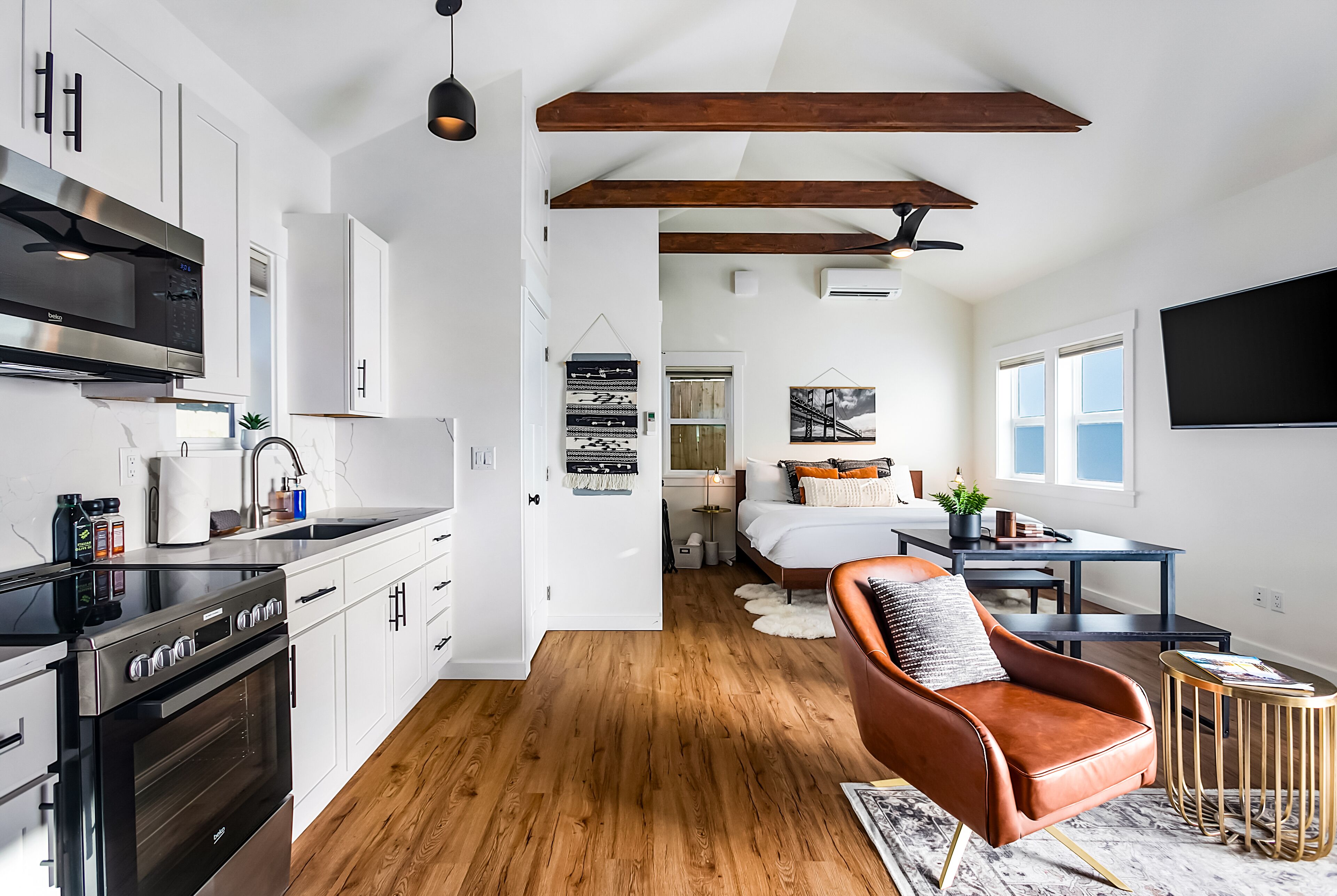 A modern kitchen with stainless steel appliances, a wooden floor, and a dining area with a leather chair and a small round table.