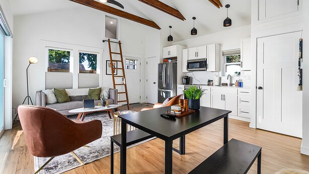 A spacious living area with a modern kitchen, wooden beams on the ceiling, and a dining table with a plant centerpiece. - Walk to the waterfront The South Sound  (Tacoma)