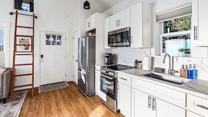 A modern kitchen with white cabinets, stainless steel appliances, a wooden ladder, and a view of the outdoors. - Walk to the waterfront The South Sound  (Tacoma)