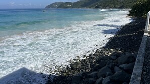 A rocky beach with clear turquoise water and a view of a mountainous landscape in the background.