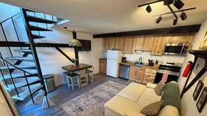 Eine moderne Küche mit Holzausstattung, einer eingebauten Mikrowelle und einem Herd. Ein Essbereich mit Tisch und Stühlen lädt zum Verweilen ein, und eine Treppe führt auf eine obere Ebene.