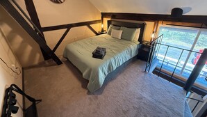 Ein Schlafzimmer mit Bett, Nachttisch, Lampe, einem Fenster mit Ausblick und einer Wanduhr.