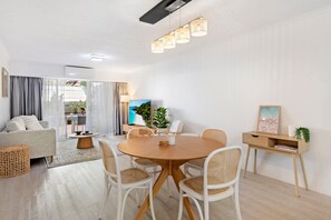 A modern living room with a round wooden table, white chairs, a sofa, and a dining area.