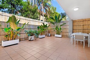 Eine Außenpatio-Terrasse mit Fliesenböden, weißen Möbeln und verschiedenen Kübelpflanzen.