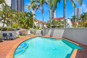 A swimming pool with a curved edge, surrounded by palm trees and a white wall.