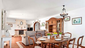 Un coin repas avec une table ronde en bois, six chaises et un lustre.