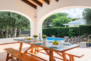 A poolside dining area with a wooden table set for six, overlooking a swimming pool and a garden. - 4 Bedroom Villa, Pool, 500m to Beach, Cala en Blanes (Cala en Blanes)