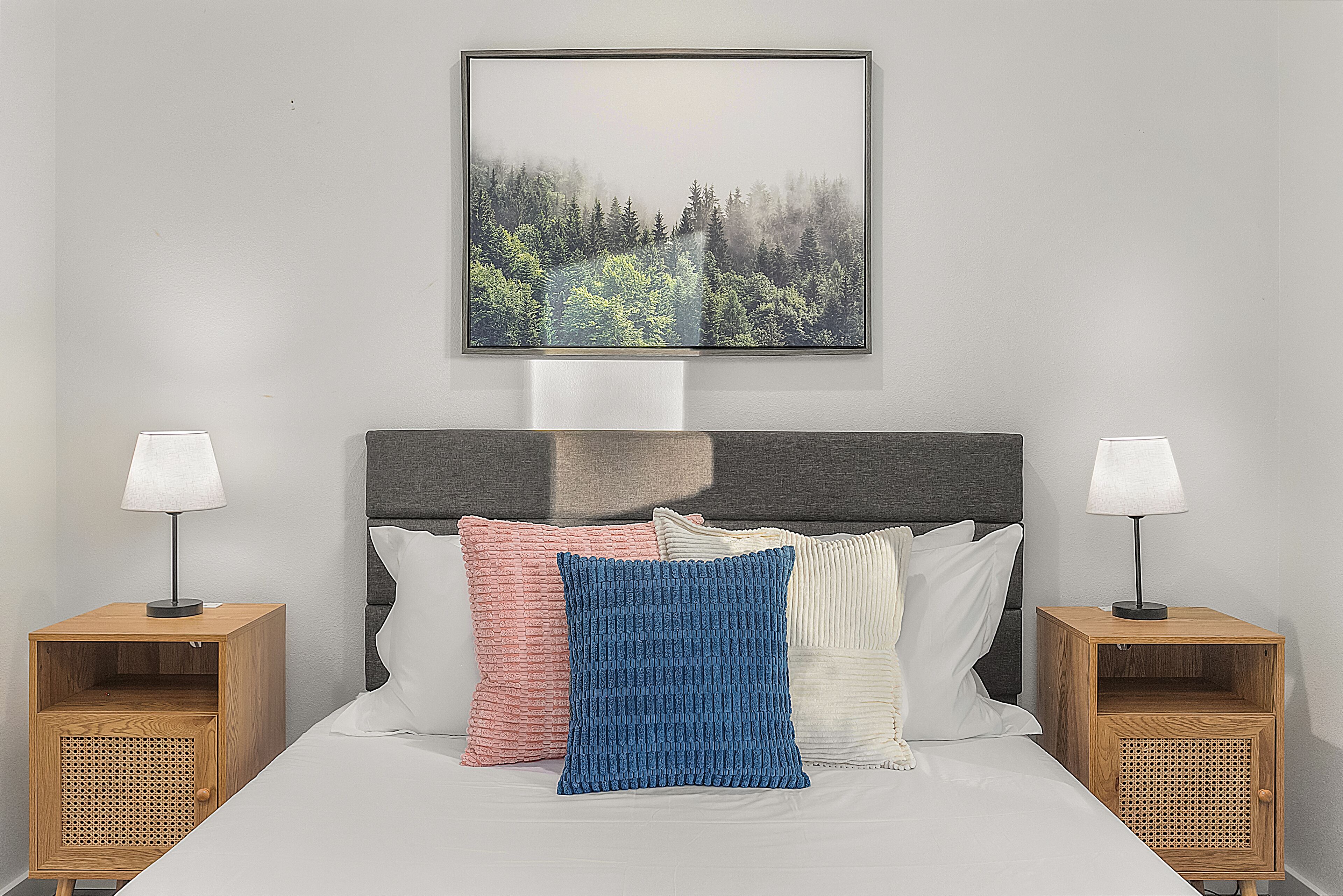 A neatly made bed with a grey headboard, flanked by two bedside tables with lamps, and a framed picture above.