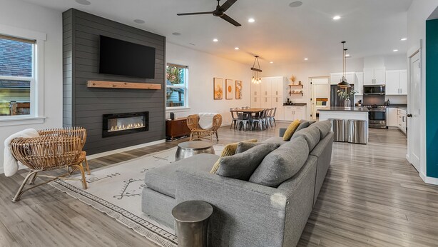 A modern living room with a fireplace, grey sofa, wicker chairs, and a dining area with a table and chairs. - Walk to the waterfront- Charmwood House  (Tacoma)