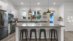 A modern kitchen with white cabinets, stainless steel appliances, and a central island with bar stools. - Walk to the waterfront- Charmwood House  (Tacoma)
