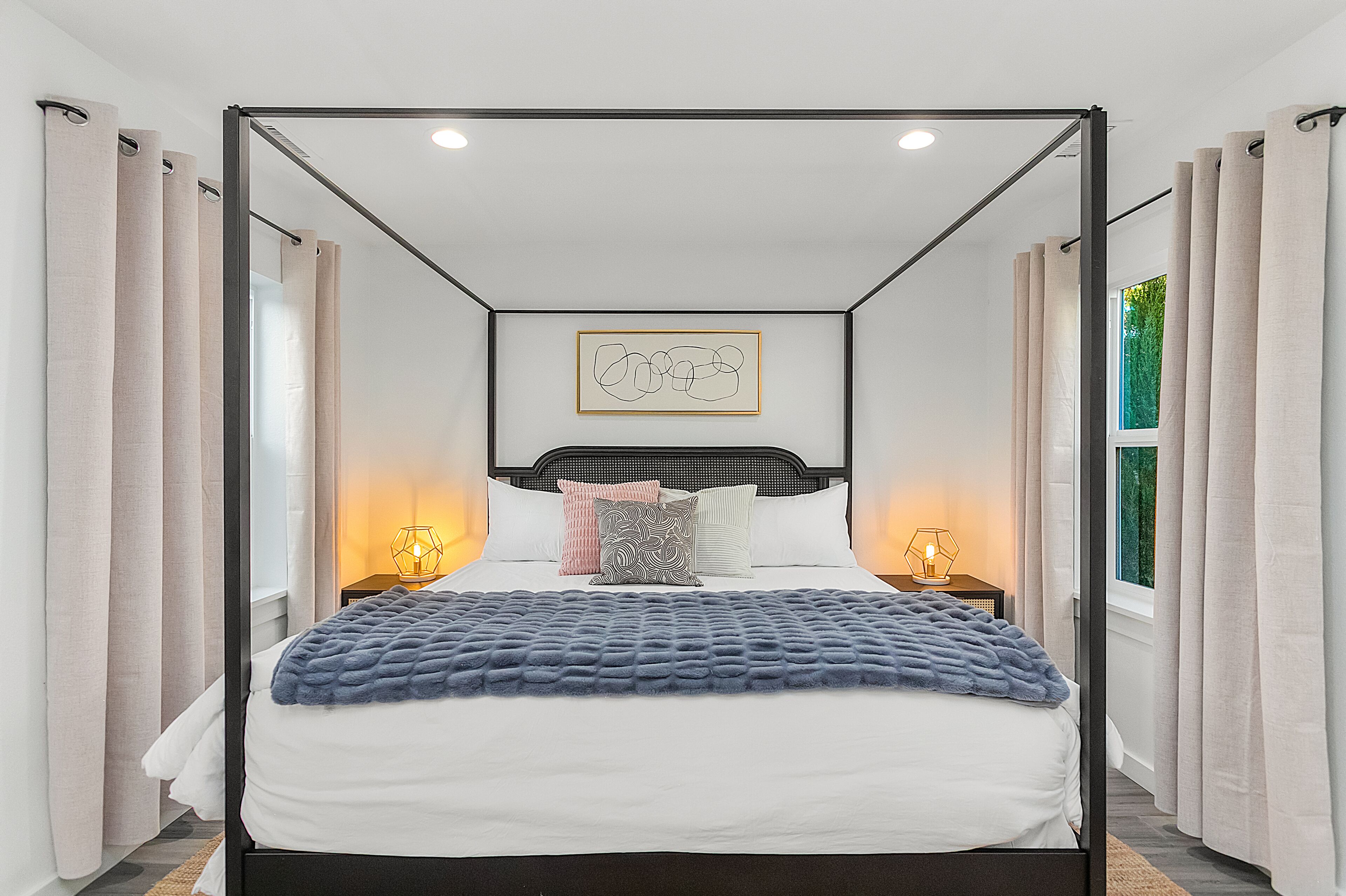 Een moderne slaapkamer met een hemelbed, een geometrisch kunstwerk aan de muur en uitzicht op groen.