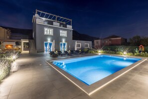 A modern house with a swimming pool, outdoor seating, and a well-lit entrance.