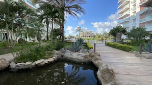 A landscaped area with a small pond, palm trees, and a pathway leading to a building. - Pacifika Marina Mazatlan by Partnerhost (Mazatlán)