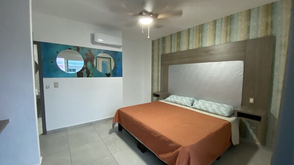 A bedroom with a bed, a ceiling fan, a wall-mounted air conditioner, and a decorative mirror.