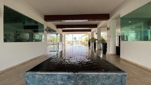 A modern hotel corridor with a reflective water feature, glass walls, and a central seating area. - Pacifika Marina Mazatlan by Partnerhost (Mazatlán)
