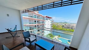 A balcony with wicker furniture, a hammock, and a view of a swimming pool and buildings. - Pacifika Marina Mazatlan by Partnerhost (Mazatlán)