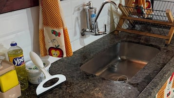 A kitchen with a granite countertop, stainless steel sink, and a window with curtains.