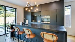 A modern kitchen with a large island, bar stools, a built-in oven, and a pendant light.