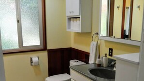 Casa de banho pequena com sanita, lavatório e espelho. Tem uma janela com vidro jateado e uma toalha pendurada na parede.