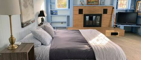 Een slaapkamer met een bed, een lamp, een televisie, een open haard en een boekenplank.