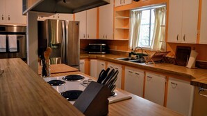 Cozinha moderna com eletrodomésticos de aço inoxidável, bancadas de madeira e uma janela com cortinas.