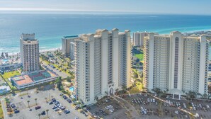 A high-rise hotel with multiple floors, a parking lot, and a view of the ocean. - •Beach Access•Pools•Gulf View•Balcony•Beach Gear•King•5min Walk to Beach•W/D•Gym (Miramar Beach)