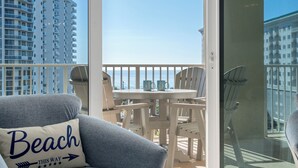 A balcony with a view of high-rise buildings, a round table with chairs, and a blue chair with a pillow labeled "Beach". - •Beach Access•Pools•Gulf View•Balcony•Beach Gear•King•5min Walk to Beach•W/D•Gym (Miramar Beach)