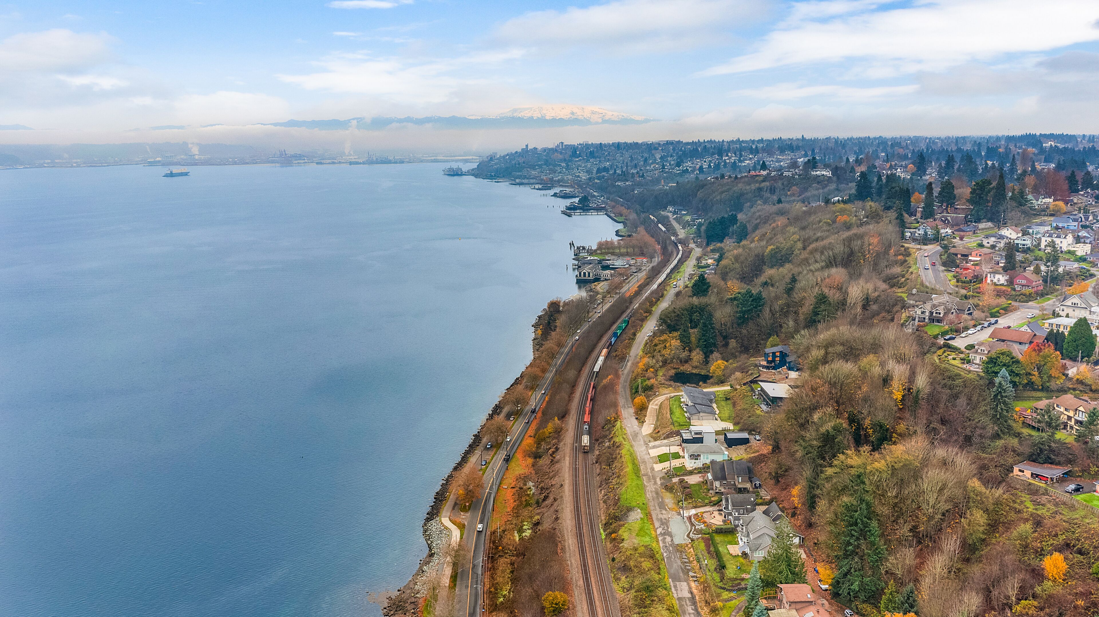 A coastal town with a railway running parallel to the waterfront, houses, and a mountain in the background.