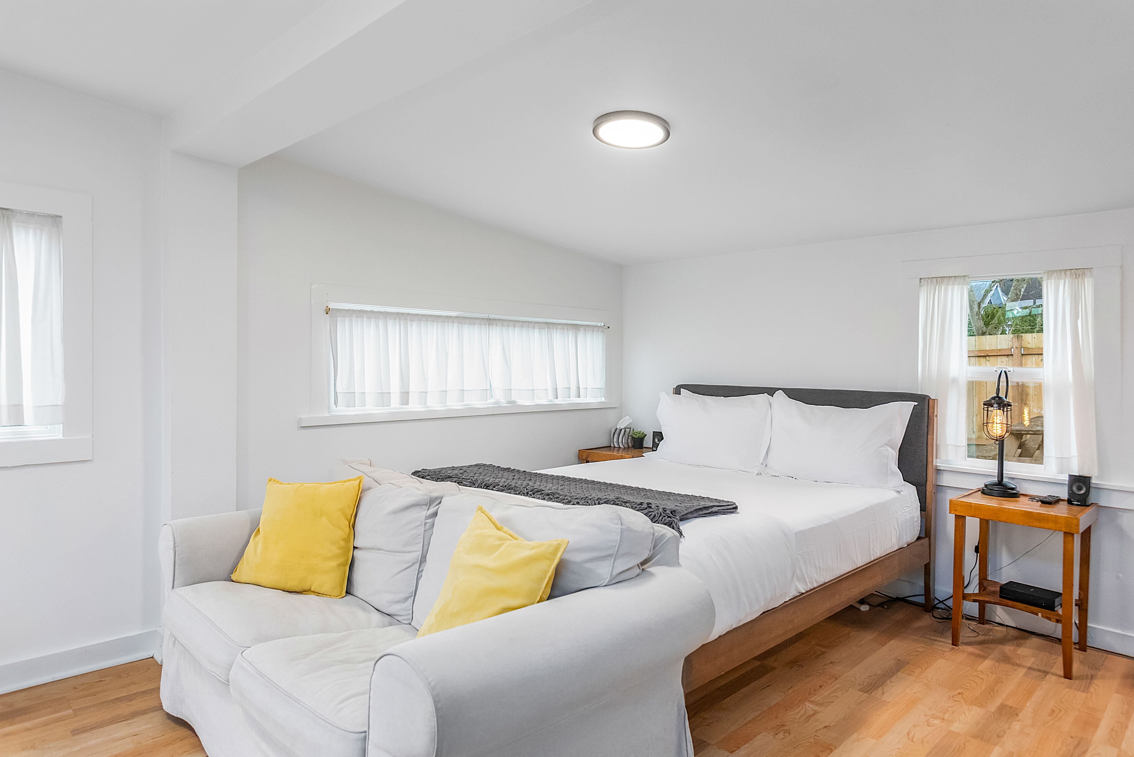 A bedroom with a bed, a sofa, a bedside table, and a window.