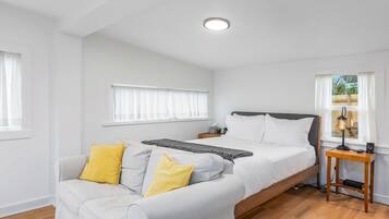 A bedroom with a bed, a sofa, a bedside table, and a window.