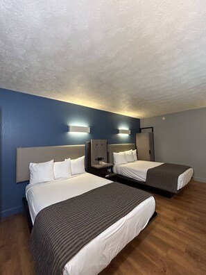 A hotel room with two beds, a wooden floor, and a blue wall. - Rodeway Inn (Emporia)
