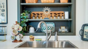 Een keuken met een roestvrijstalen spoelbak, planken met glazen en een decoratieve lamp in de vorm van een zon.