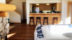 Et moderne interiør med et køkkenområde, trægulv, en trappe og en siddeplads med sofa og puder.