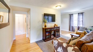 A living room with a wooden floor, a brown leather sofa, a dark wood cabinet, and a flat-screen TV mounted on the wall.